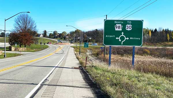 A green sign with directions for routes and a visual representation of the roundabout exits